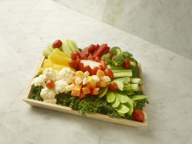 Vegetable Crudité Platter Featuring Assorted Raw Vegetables and Veggie Sticks on a Bed of Kale with a Red Pepper Tulip Cup of Creamy Dipping Sauce on a Square Wood Serving Tray on a Marble Surface