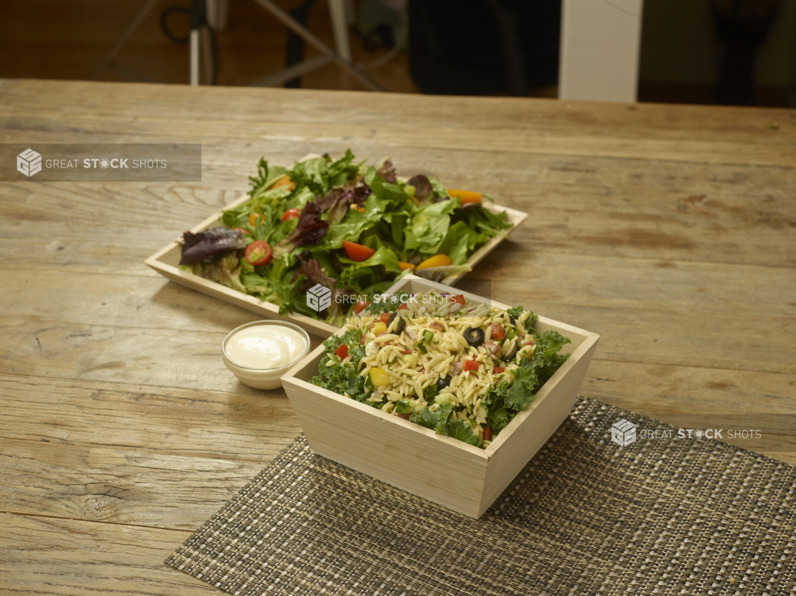 Catering Salad Combo with Spring Mix Salad and Orzo Pasta Salad in Wood Serving Trays with a Creamy Dressing on a Wooden Table