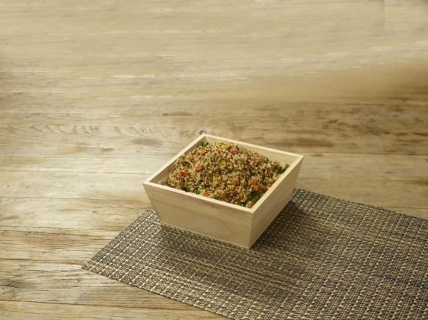 A Small Deep Square Wood Serving Tray of Quinoa Salad on a Woven Placemat on a Rustic Wood Surface in an Indoor Setting