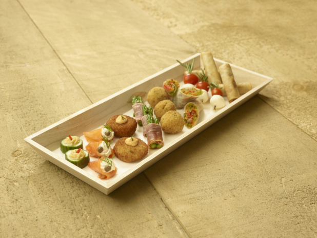 A Narrow Rectangular Wood Serving Tray with Assorted Passed Appetizers (Smoked Salmon Rolls, Croquettes, Spring Rolls, Cucumber Bites, Caprese Skewers) for Catering on an Untreated Wood Surface - Variation
