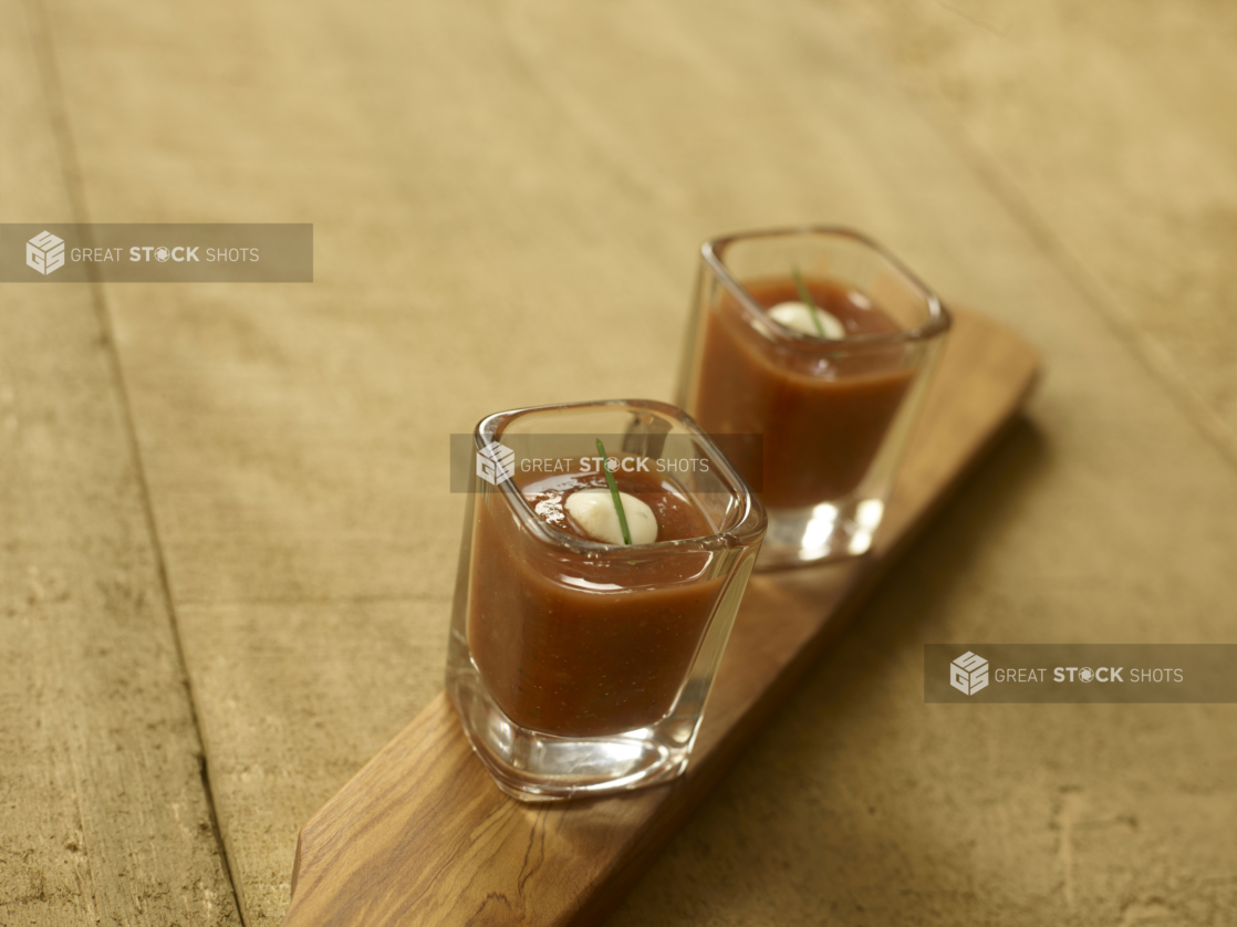 Two Shot Glasses of Cold Gazpacho Soup on a Wooden Paddle on a Wooden Table - for Catering