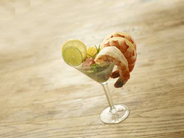Black Tiger Shrimp Cocktail in a Martini Glass with Fresh Vegetables and Citrus Fruit Garnish on a Rustic Wooden Surface in an Indoor Setting