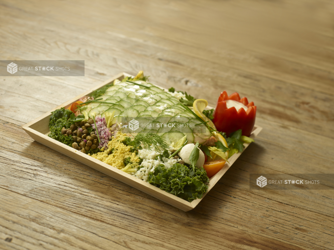 Rectangular Wood Serving Tray with Poached Salmon and Cucumber Scales with Assorted Fresh Vegetables and Salads for Catering on a Rustic Wooden Surface in an Indoor Setting