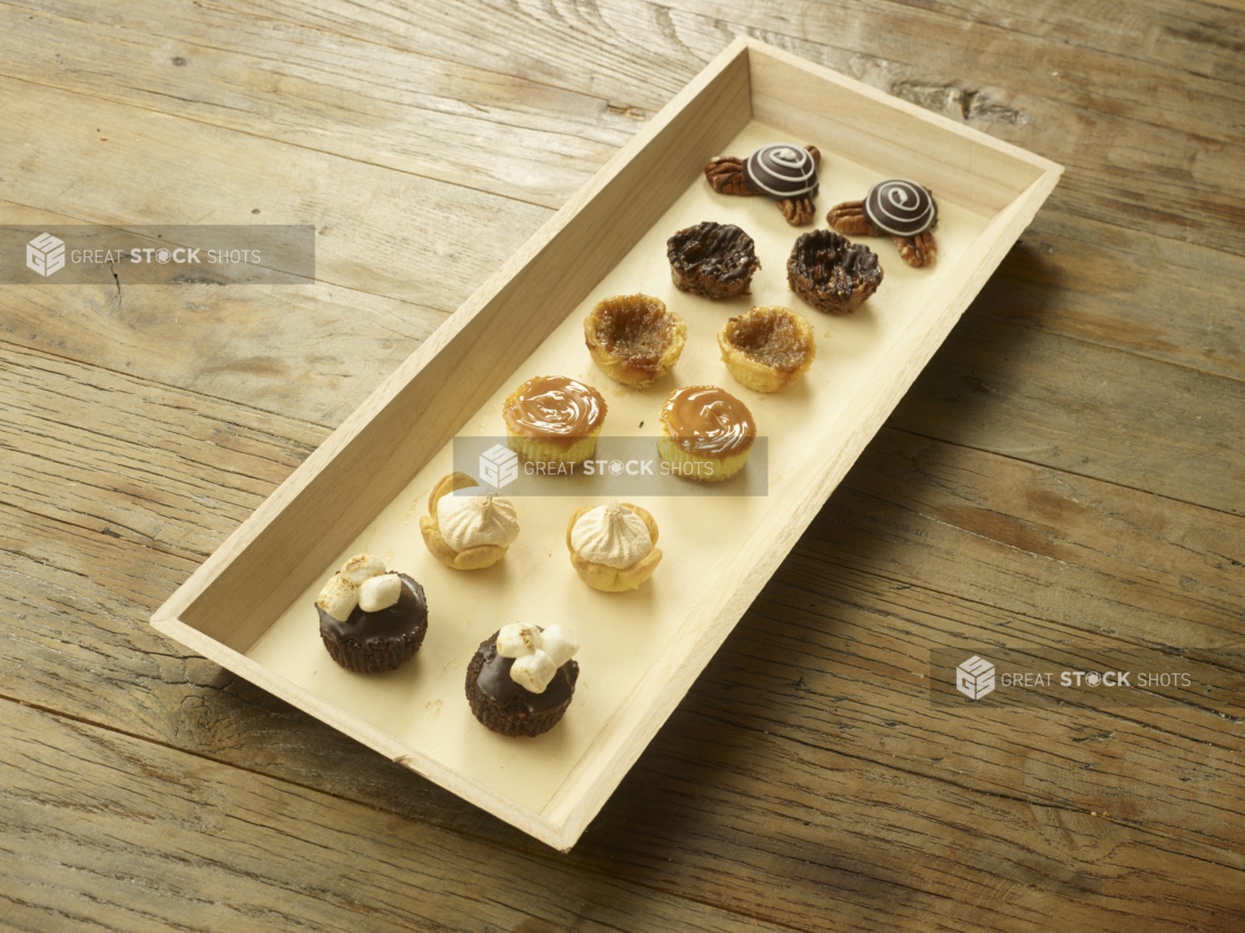 Assorted Mini Tarts and Cakes on a Narrow Rectangular Wood Tray on a Wooden Table - for Catering