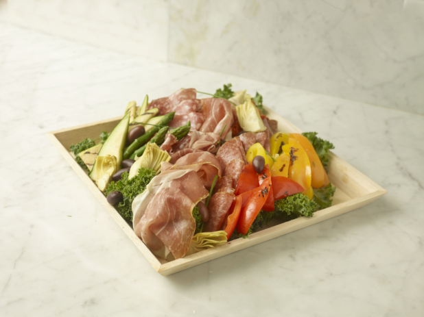 Antipasto Tray Featuring Italian Cold Cuts, Roasted Peppers, Grilled Vegetables and Artichoke Hearts on a Bed of Kale in a Square Wood Serving Tray on a Marble Surface