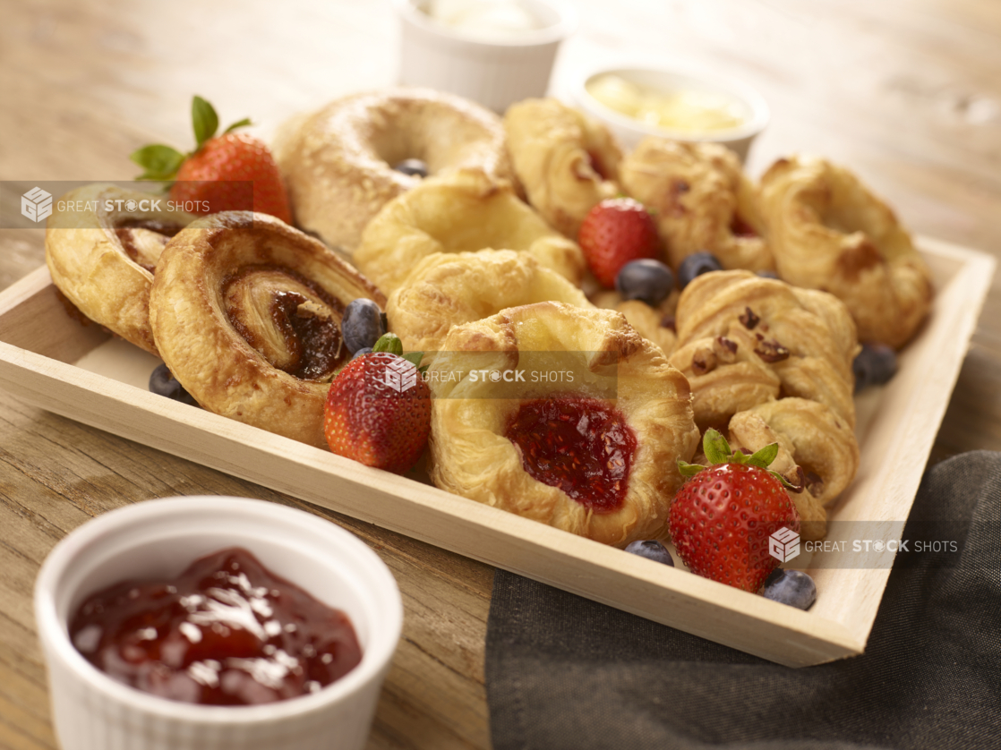 Square Wooden Tray with Assorted Danishes, Cinnamon Rolls and Bagels on a Wooden Table with Jam and Butter - for Breakfast Catering