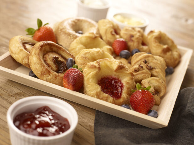Square Wooden Tray with Assorted Danishes, Cinnamon Rolls and Bagels on a Wooden Table with Jam and Butter - for Breakfast Catering