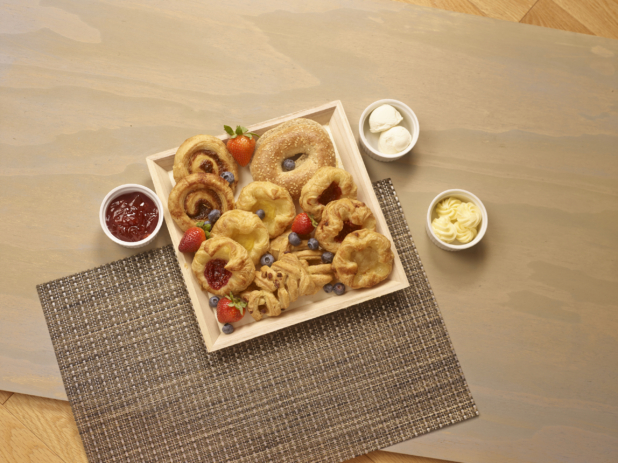 Overhead View of Square Wooden Tray with Assorted Danishes, Cinnamon Rolls and Bagels on a Wooden Table with Jam and Butter – for Breakfast Catering