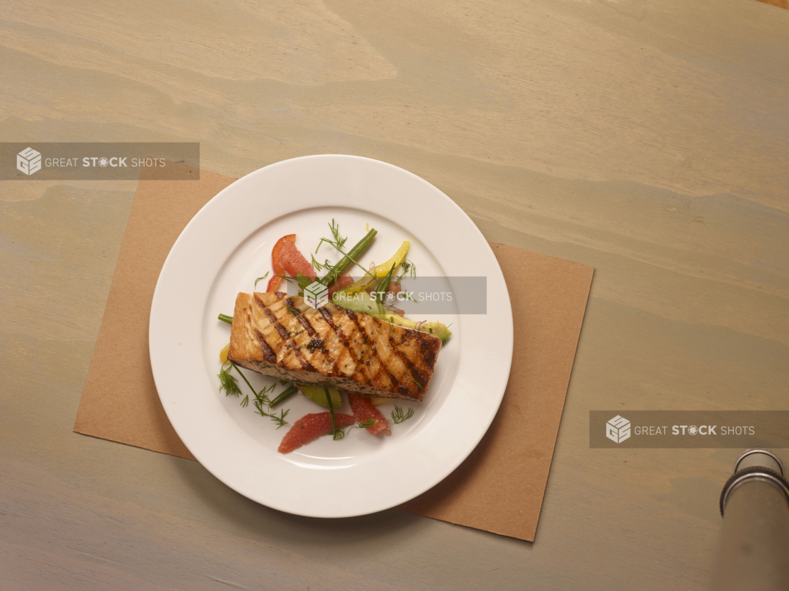 Overhead View of a Round White Dinner Plate of Grilled Salmon on a Bed of Grapefruit, Avocado and Green Beans on a Wooden Surface