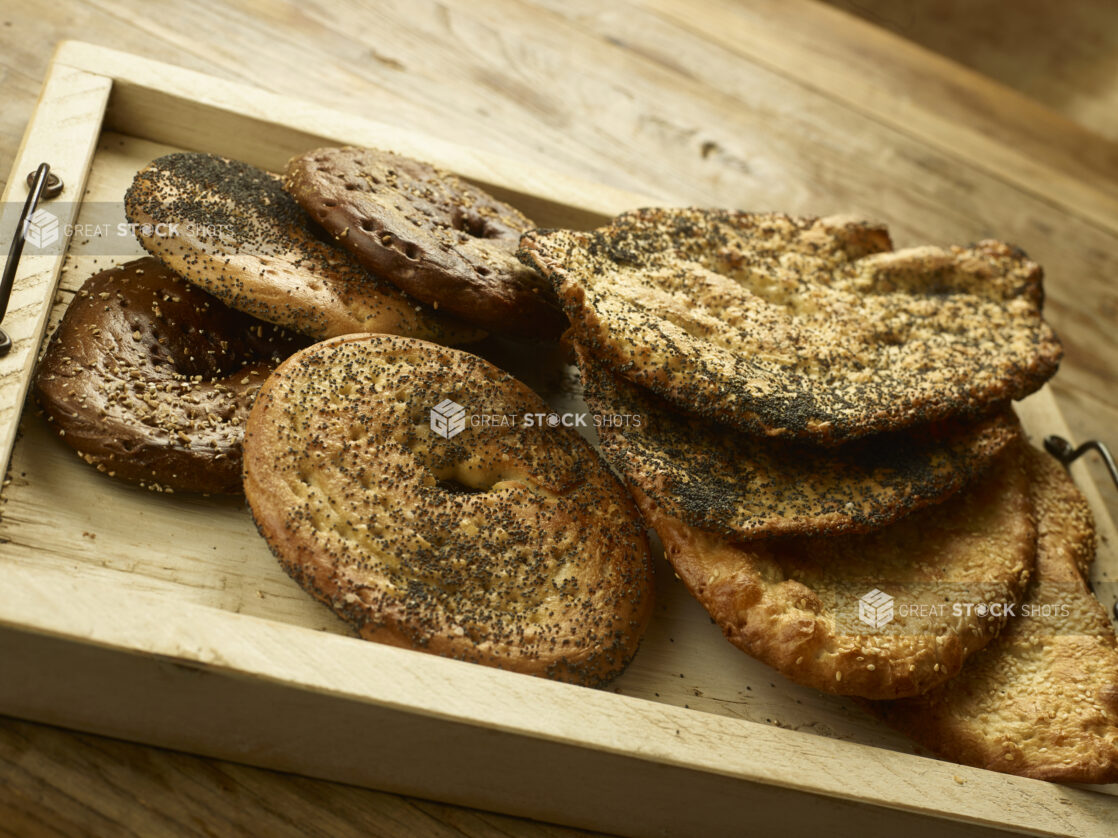 Assorted New York flat bagels and breads in a wooden tray on a wooden background