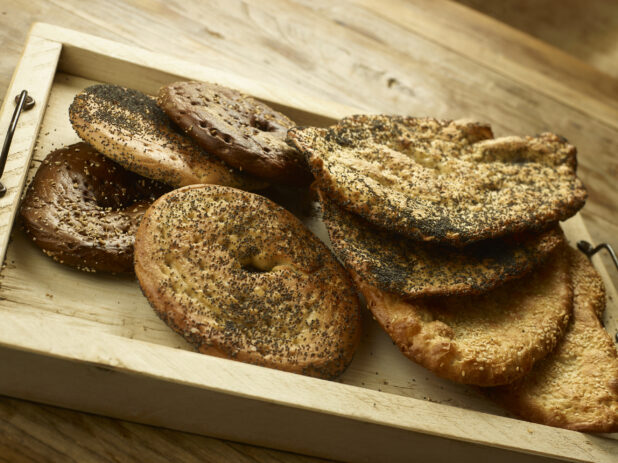 Assorted New York flat bagels and breads in a wooden tray on a wooden background