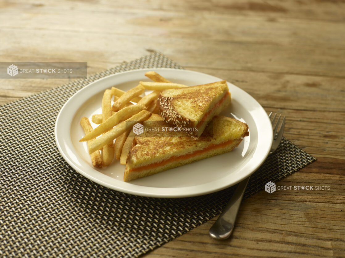 Grilled cheese on egg bread with french fries on a white round plate on a wooden background