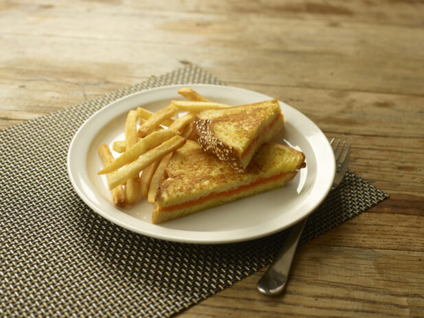 Grilled cheese on egg bread with french fries on a white round plate on a wooden background