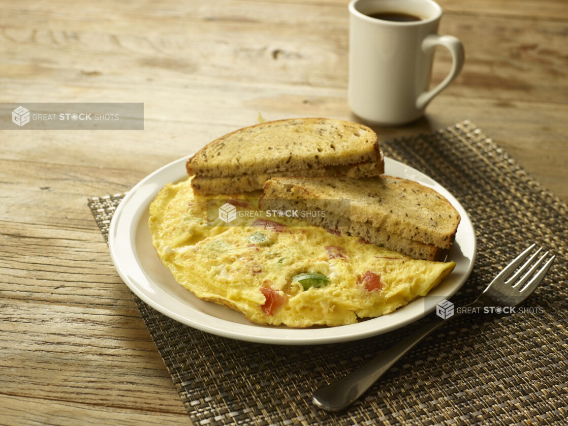 Vegetarian omelette with caraway seed rye toast on a white plate with a fork and a cup of coffee in the background