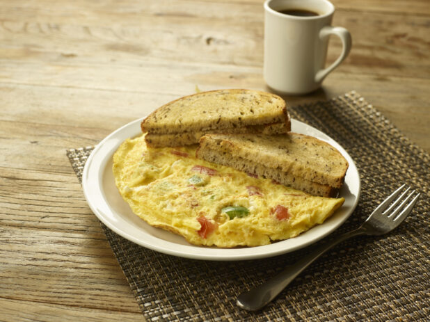 Vegetarian omelette with caraway seed rye toast on a white plate with a fork and a cup of coffee in the background