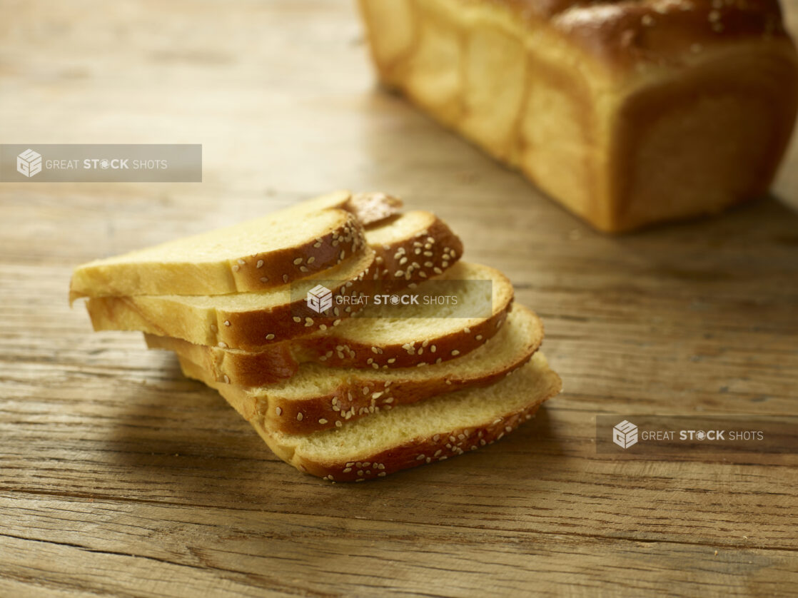 Challah bread, egg bread, sliced with a whole chala in the background on a wooden background