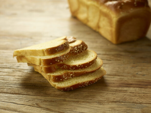 Challah bread, egg bread, sliced with a whole chala in the background on a wooden background