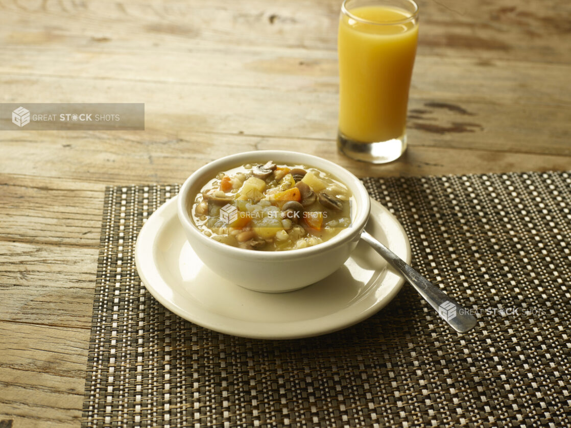 Mushroom barley soup in a cup size on a plate with a spoon with a glass of orange juice on the side