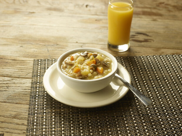 Mushroom barley soup in a cup size on a plate with a spoon with a glass of orange juice on the side