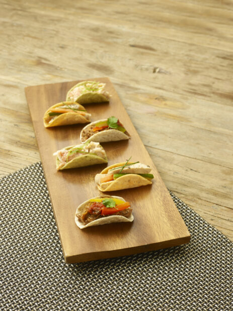 Assorted mini tacos on a wooden board on a wooden background