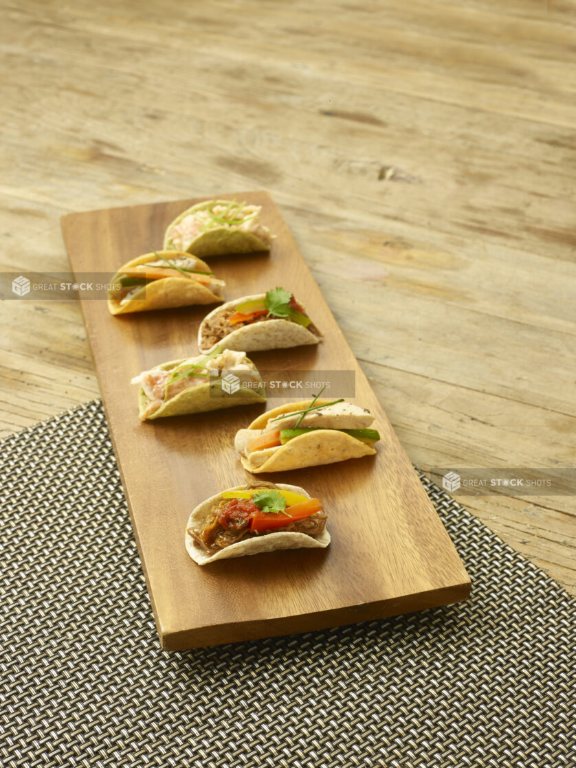 Assorted mini tacos on a wooden board on a wooden background