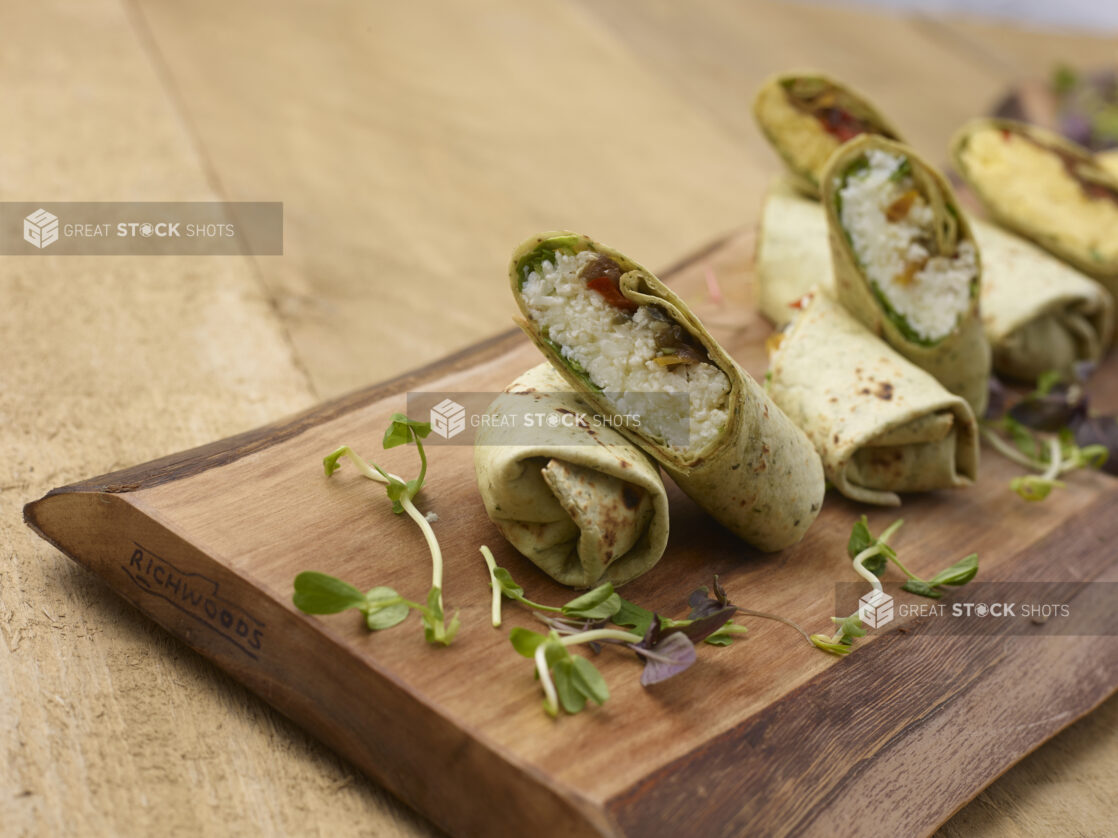 A Wooden Platter of Mini Egg White Breakfast Wraps and Regular Breakfast Wraps on a Wooden Table in an Indoor Setting