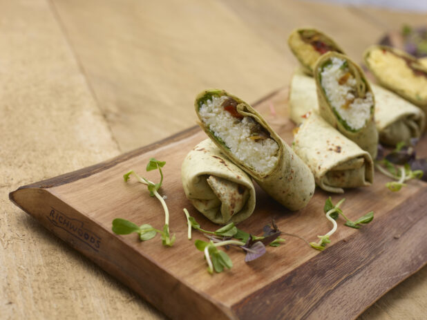 A Wooden Platter of Mini Egg White Breakfast Wraps and Regular Breakfast Wraps on a Wooden Table in an Indoor Setting