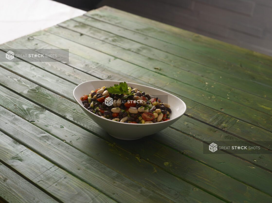 Mixed bean and corn salad in white oval bowl on a hunter green wooden background