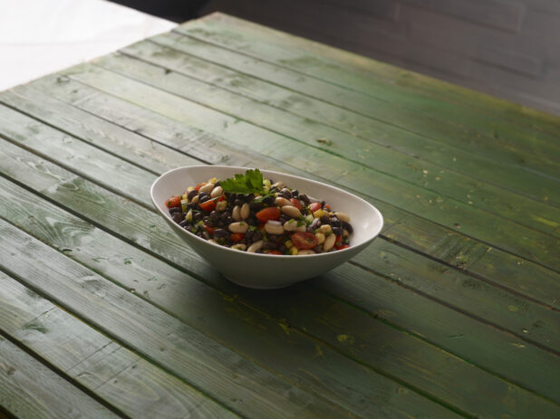 Mixed bean and corn salad in white oval bowl on a hunter green wooden background