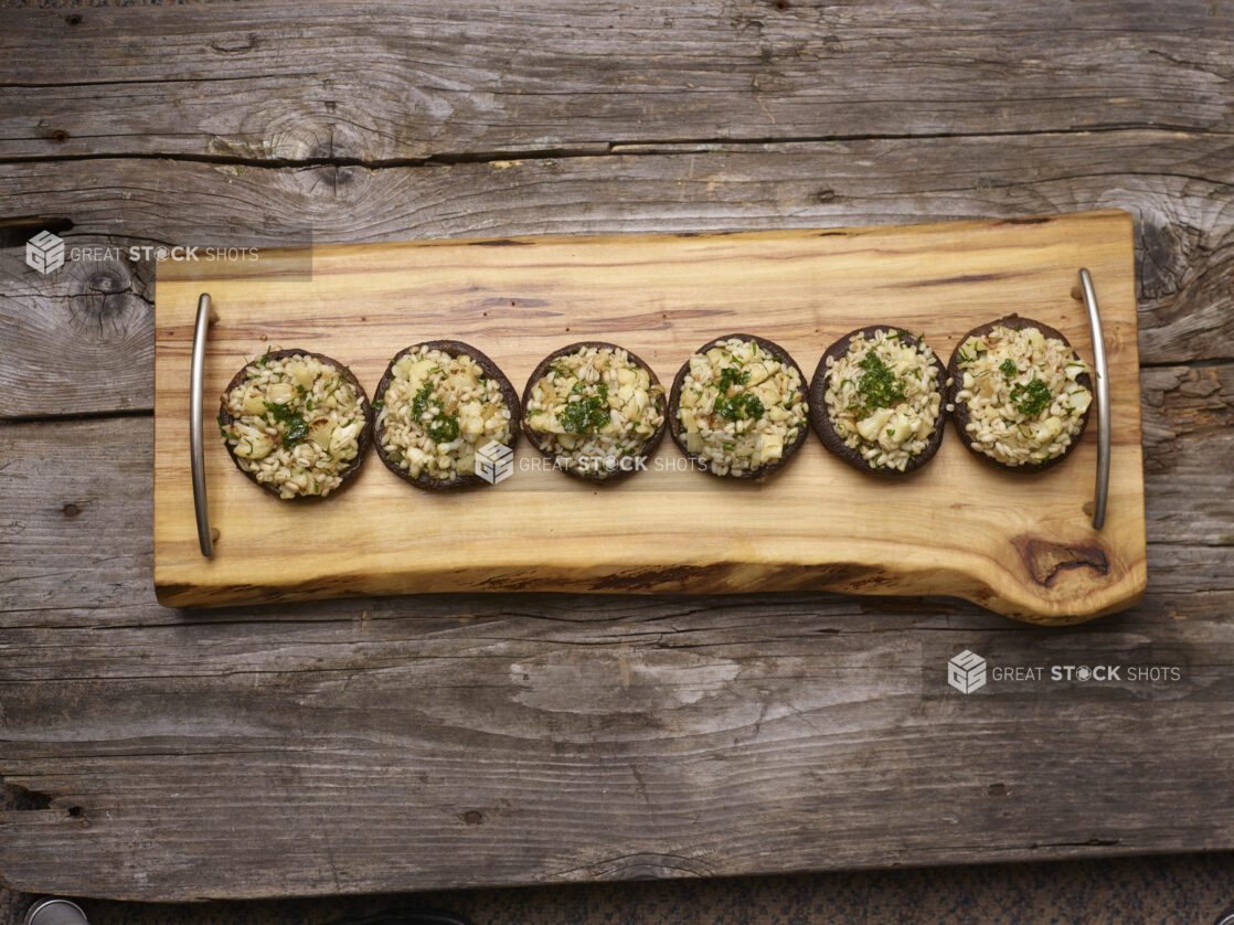 Overhead View of Stuffed Portobello Mushroom Caps on a Wood Platter Garnished with Parsley on a Rustic Wooden Surface