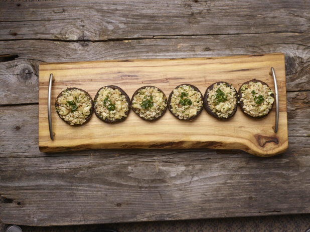 Overhead View of Stuffed Portobello Mushroom Caps on a Wood Platter Garnished with Parsley on a Rustic Wooden Surface