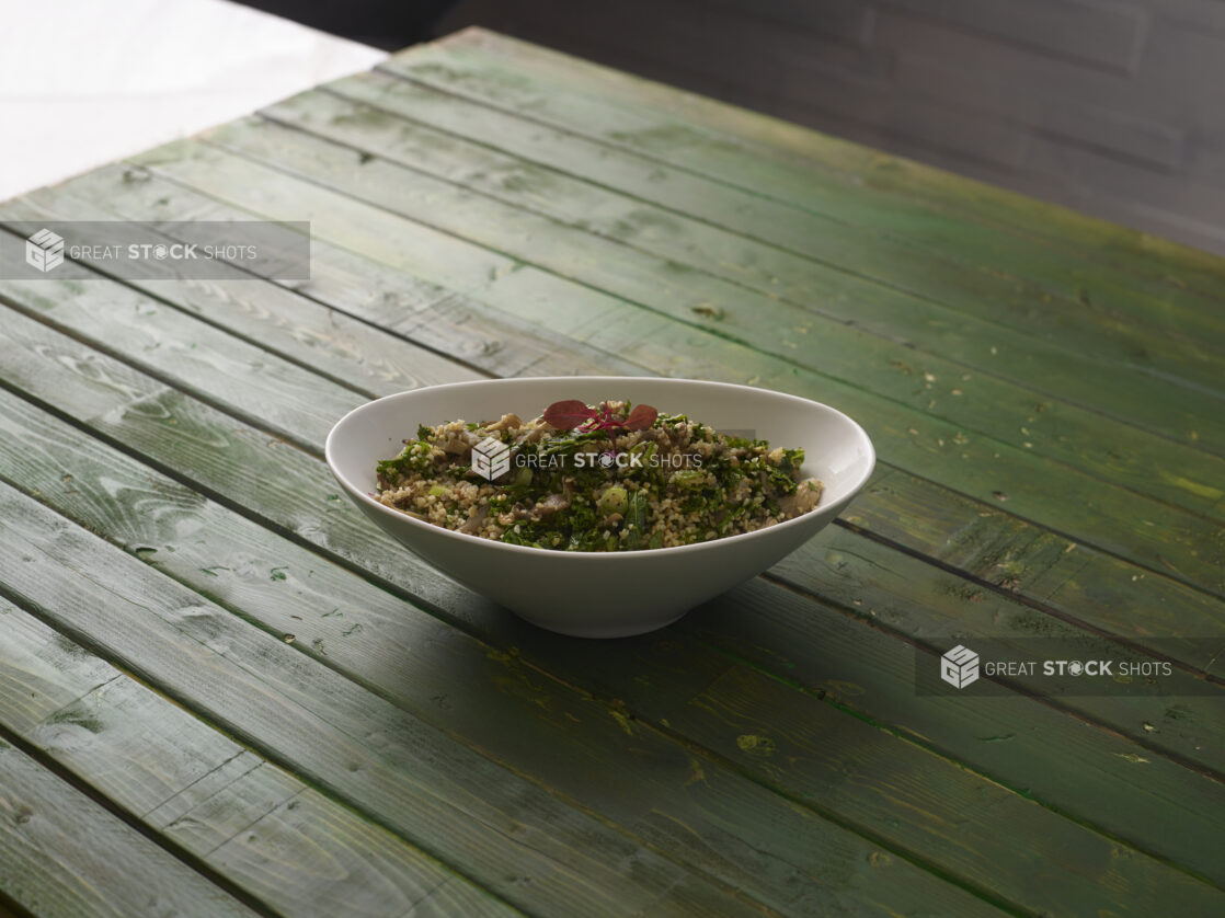 Cous cous salad in a white oval bowl on a hunter green wooden background