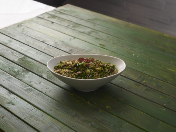 Cous cous salad in a white oval bowl on a hunter green wooden background