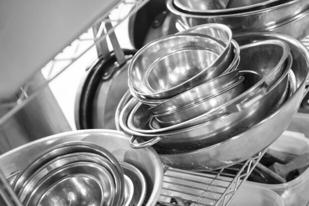 Black and white photo of kitchen mixing bowls and other restaurant equipment on a metal wire rack