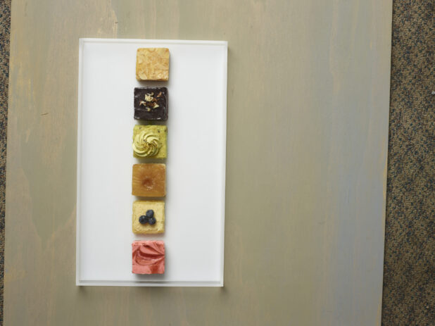 Elegant assorted mini square colourful desserts on a white rectangular platter on a wooden background