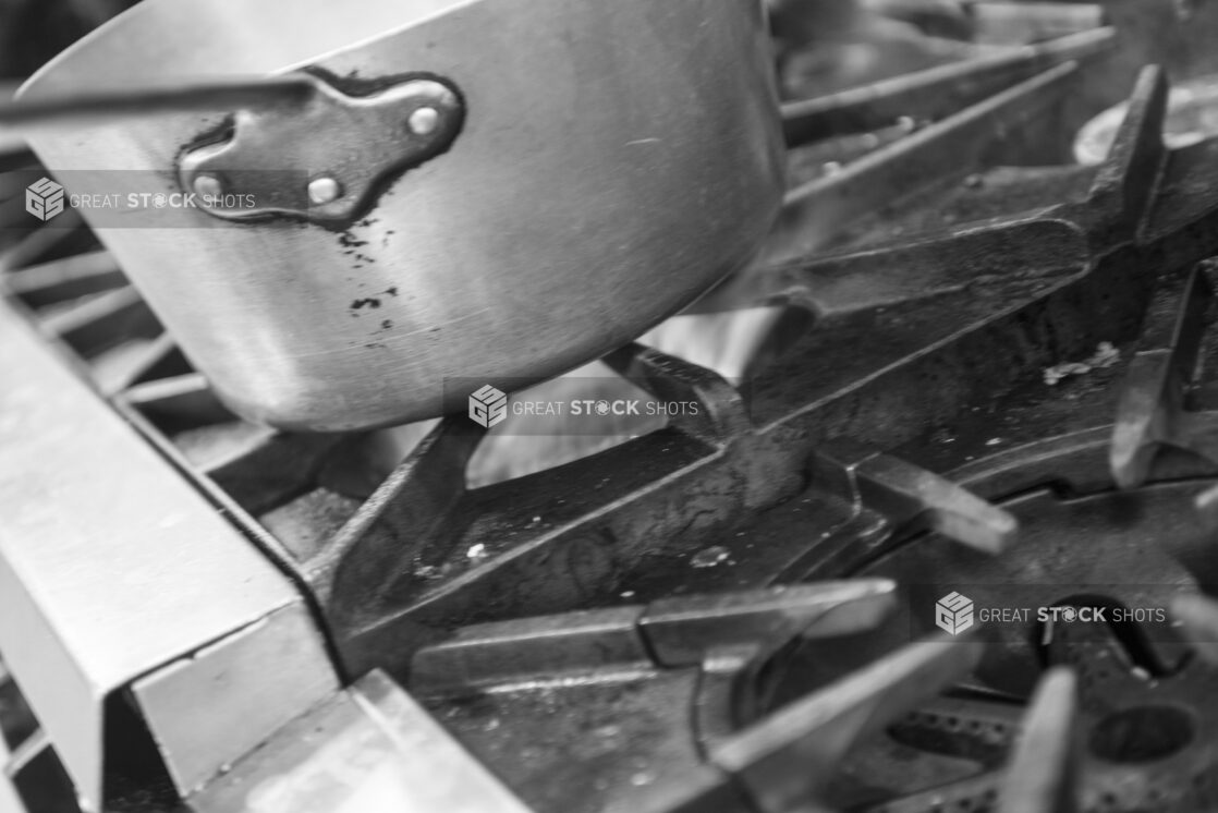 Black and white photo of a sauce pan on a gas stove, close up view