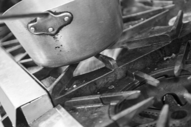 Black and white photo of a sauce pan on a gas stove, close up view
