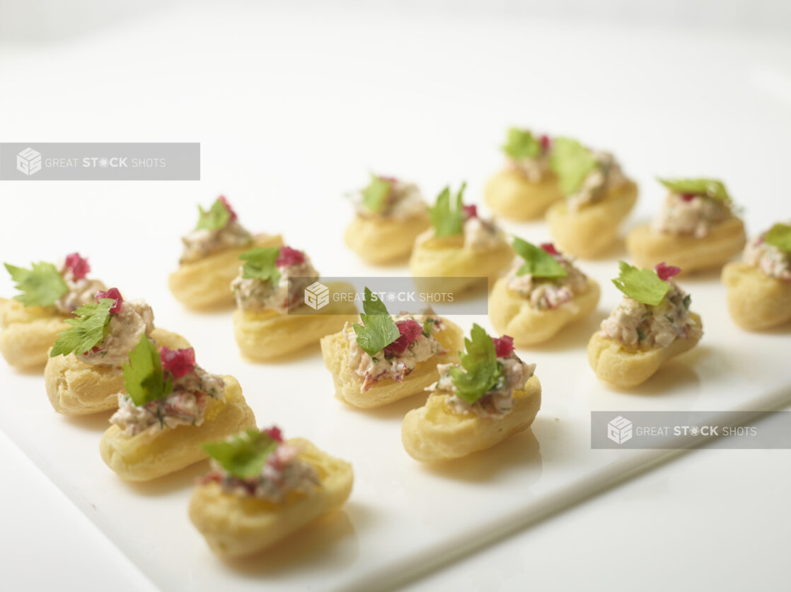 A Platter of Choux Puff Pastry Boats Stuffed with Lobster Salad and Garnished with Picked Red Beets and Parsley on a White Platter and White Table Surface