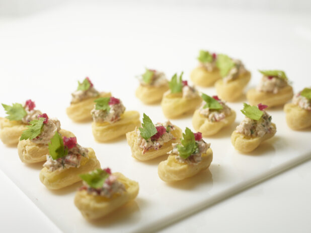 A Platter of Choux Puff Pastry Boats Stuffed with Lobster Salad and Garnished with Picked Red Beets and Parsley on a White Platter and White Table Surface