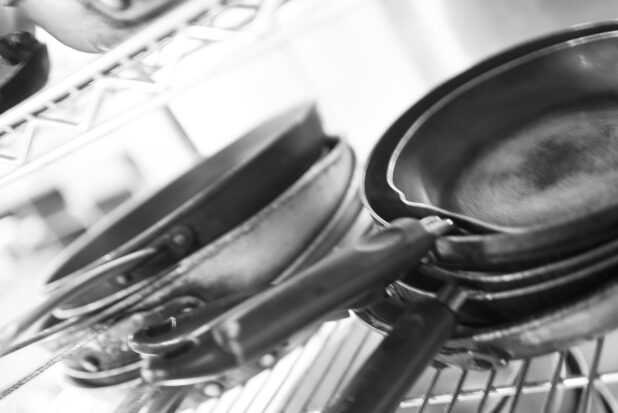 Black and white photo of kitchen pans on a metal wire rack in a restaurant kitchen