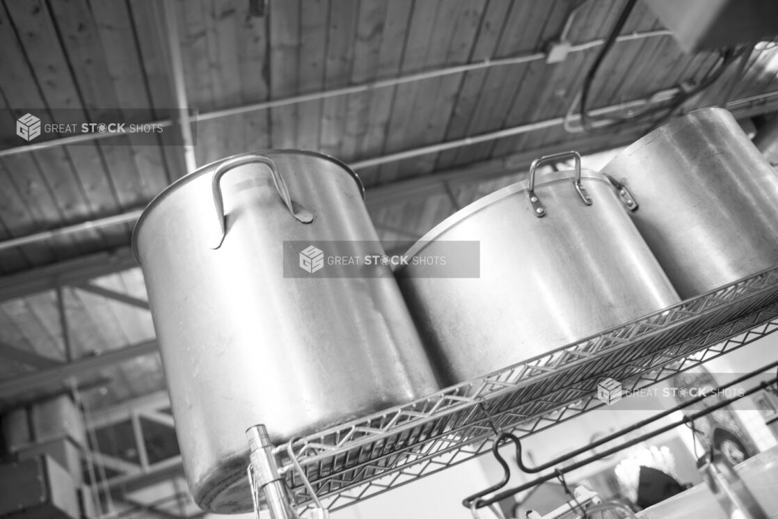 Black and white photo of stock pots in a restaurant kitchen on a metal wire rack