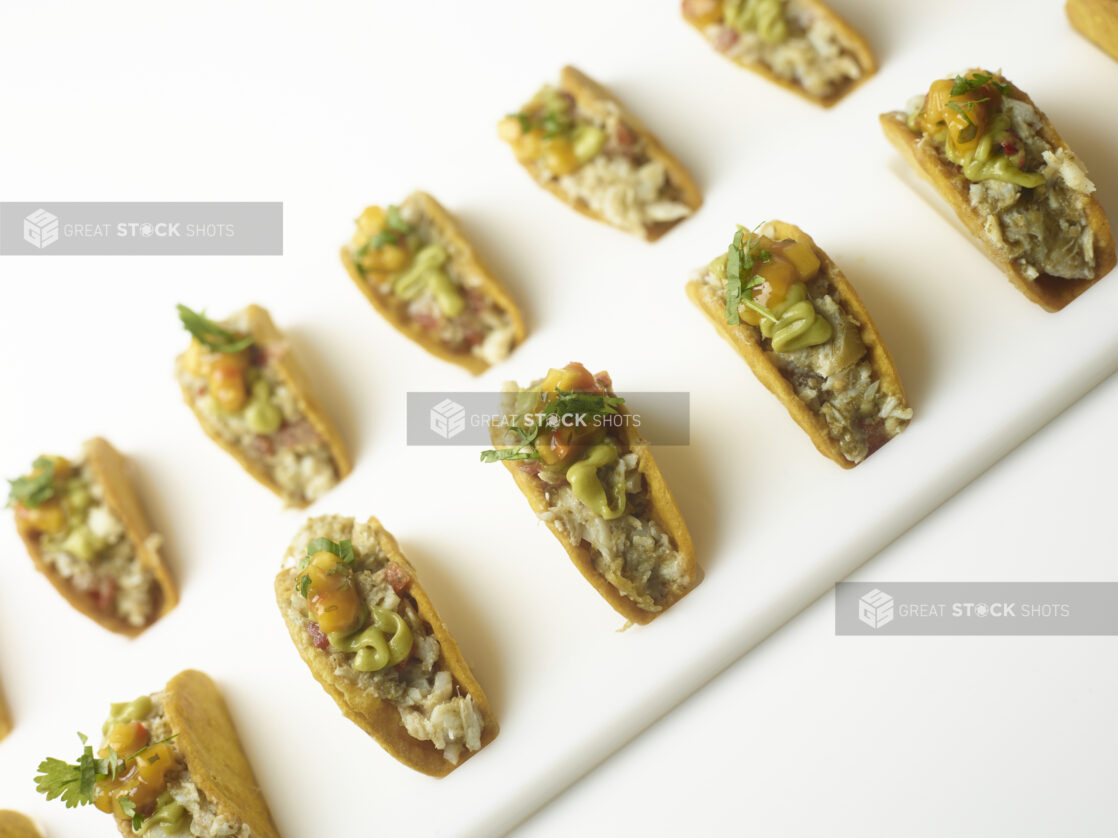 Mini fish tacos with guacamole and mango salsa on a white tray on a white background