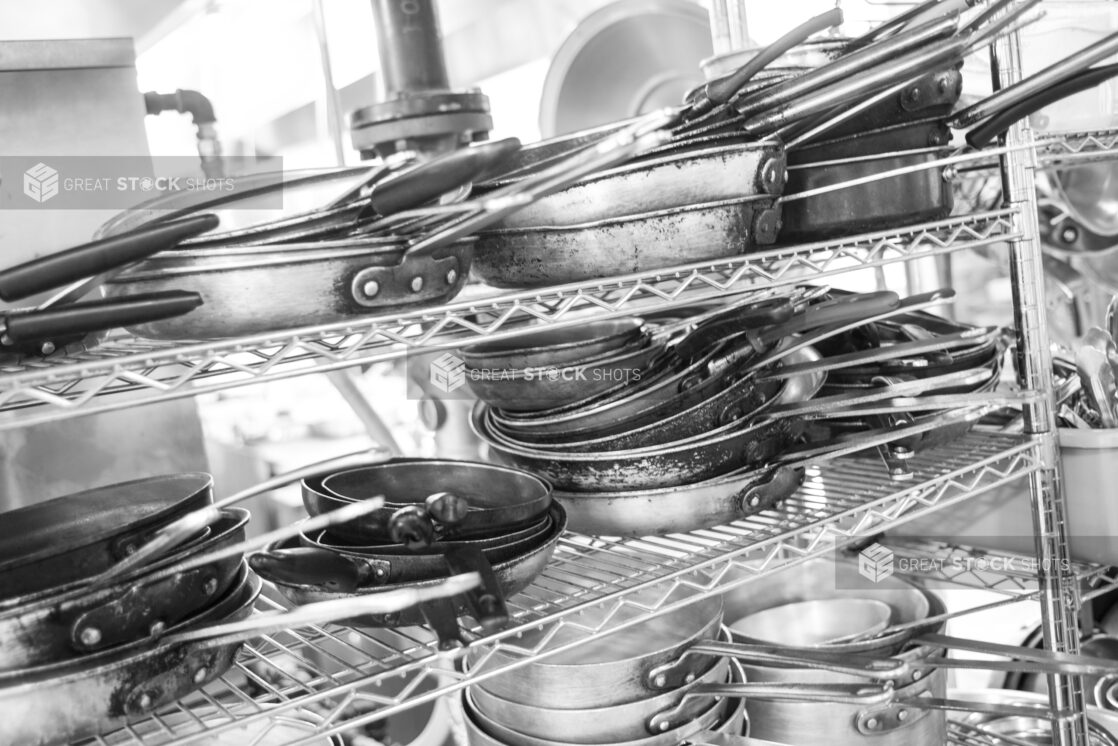 Black and white photo of pots and pans on a metal wire rack in a restaurant kitchen