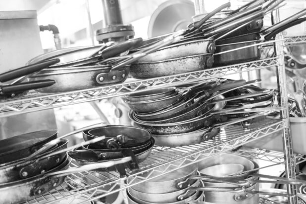 Black and white photo of pots and pans on a metal wire rack in a restaurant kitchen