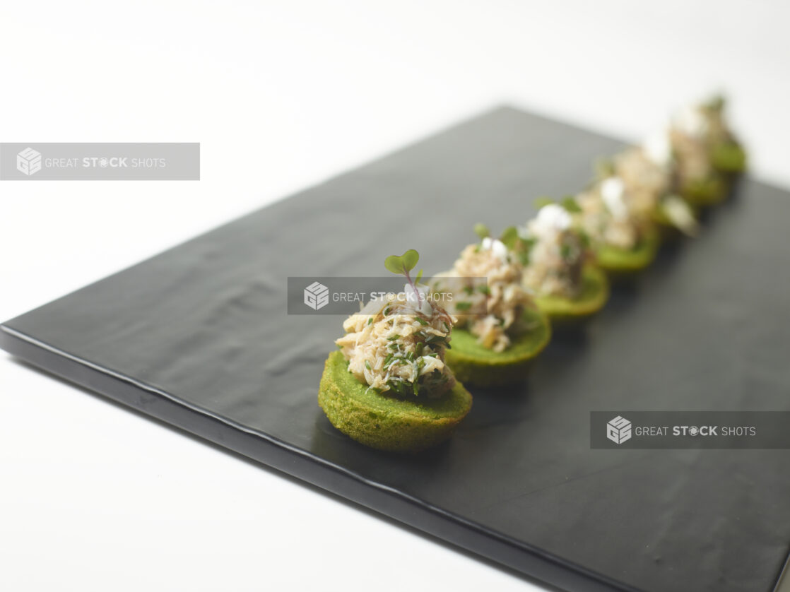 A Platter of Spinach Canapés with Crab Meat Salad and Chopped Chives on a Slate Platter on a White Table Surface