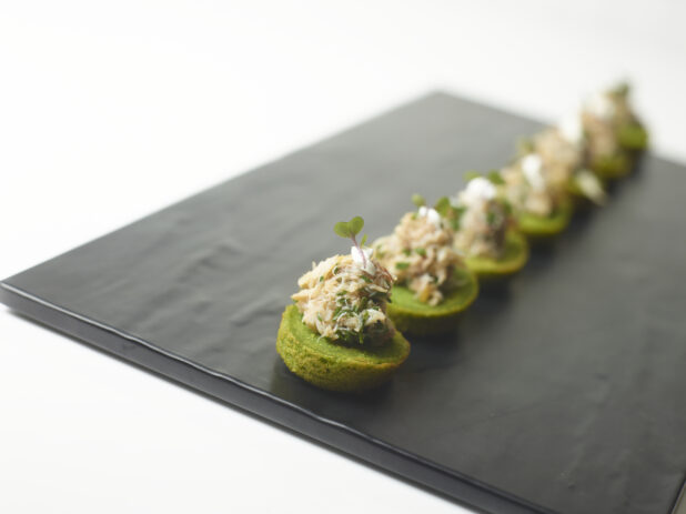 A Platter of Spinach Canapés with Crab Meat Salad and Chopped Chives on a Slate Platter on a White Table Surface