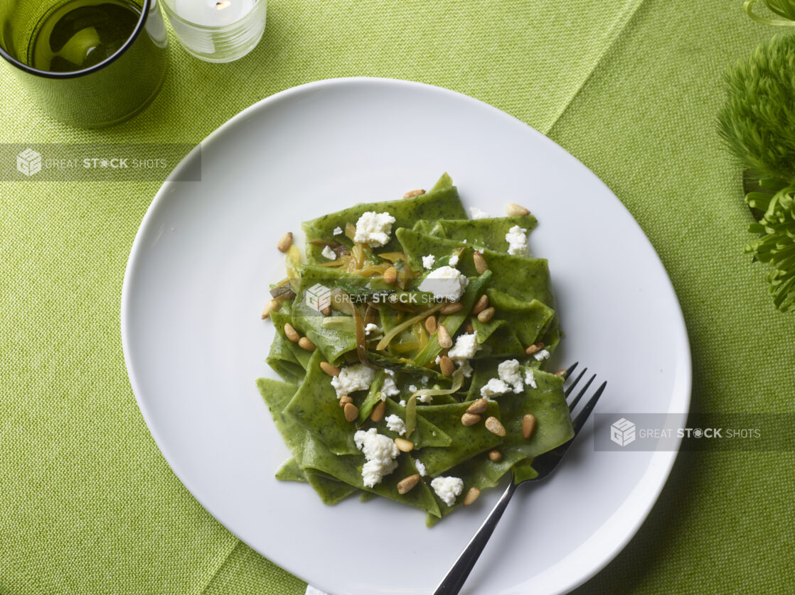 Spinach fazzoletti pasta with pine nuts, goat cheese and sauteed leeks on a white round plate on a lime green tablecloth