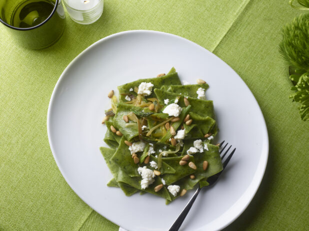 Spinach fazzoletti pasta with pine nuts, goat cheese and sauteed leeks on a white round plate on a lime green tablecloth
