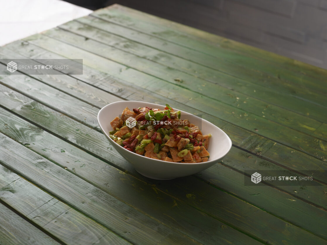 Sweet potato salad with goji berries and green beans in a white bowl on a hunter green wooden background