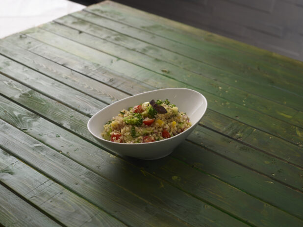 Cous cous salad with fresh vegetables on a hunter green background